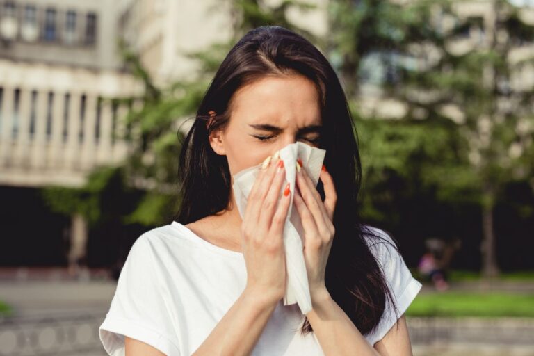 A woman outdoors blowing her nose into a tissue