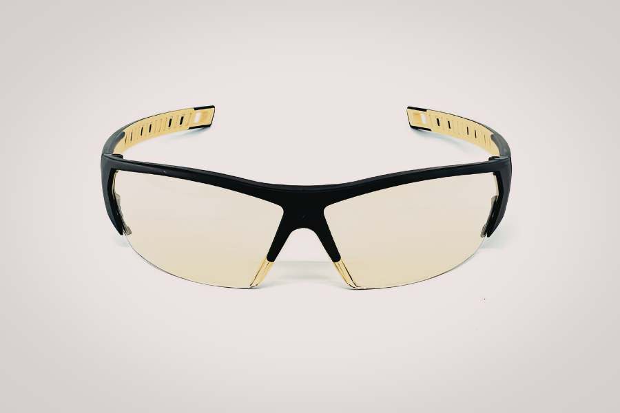 Protective eyewear featuring a sleek wraparound design with a black frame, gold accents, and lightly tinted lenses for a modern, sporty look.