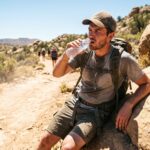 Hiker drinks water on a trail while showing signs of dehidration