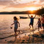 Five joyful, barefoot children running and jumping along a lake shoreline at sunset. Backlit by warm, golden light, they are splashing in the shallow water and across the sand.